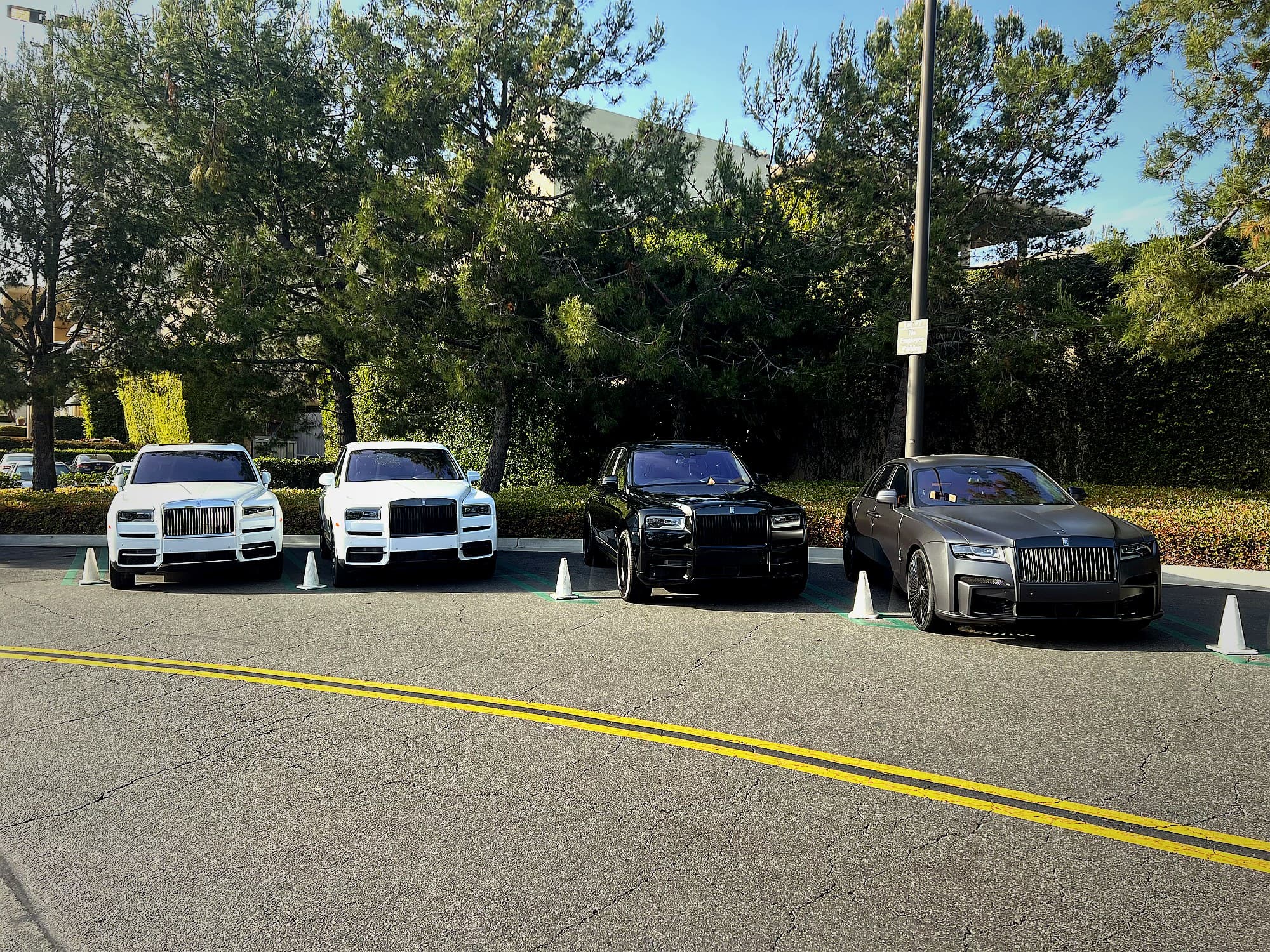 Two white Rolls-Royce Cullinans, a black Cullinan and a grey Ghost lined up in a coned-off valet bay